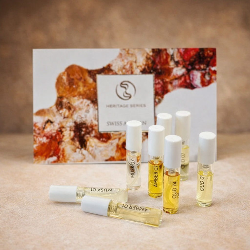 Set di campioni di fragranze della serie Swiss Arabian Heritage con diverse piccole fiale roll-on (tra cui Amber 01, Musk 07, Oud 07) in confezione trasparente, disposte davanti a una scatola decorativa su uno sfondo chiaro.